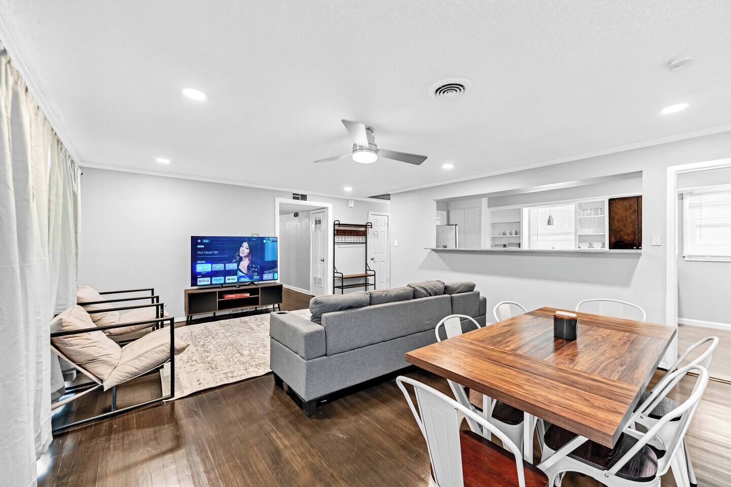 A modern living room with a sofa, TV, dining table, and a ceiling fan.
