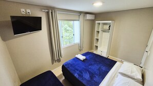 A bedroom with a bed, a TV, a window with curtains, a wardrobe, and a bedside table. - Ipê Eco Village - Apartments with Kitchen, 5 min. from Beto Carrero World (Penha)