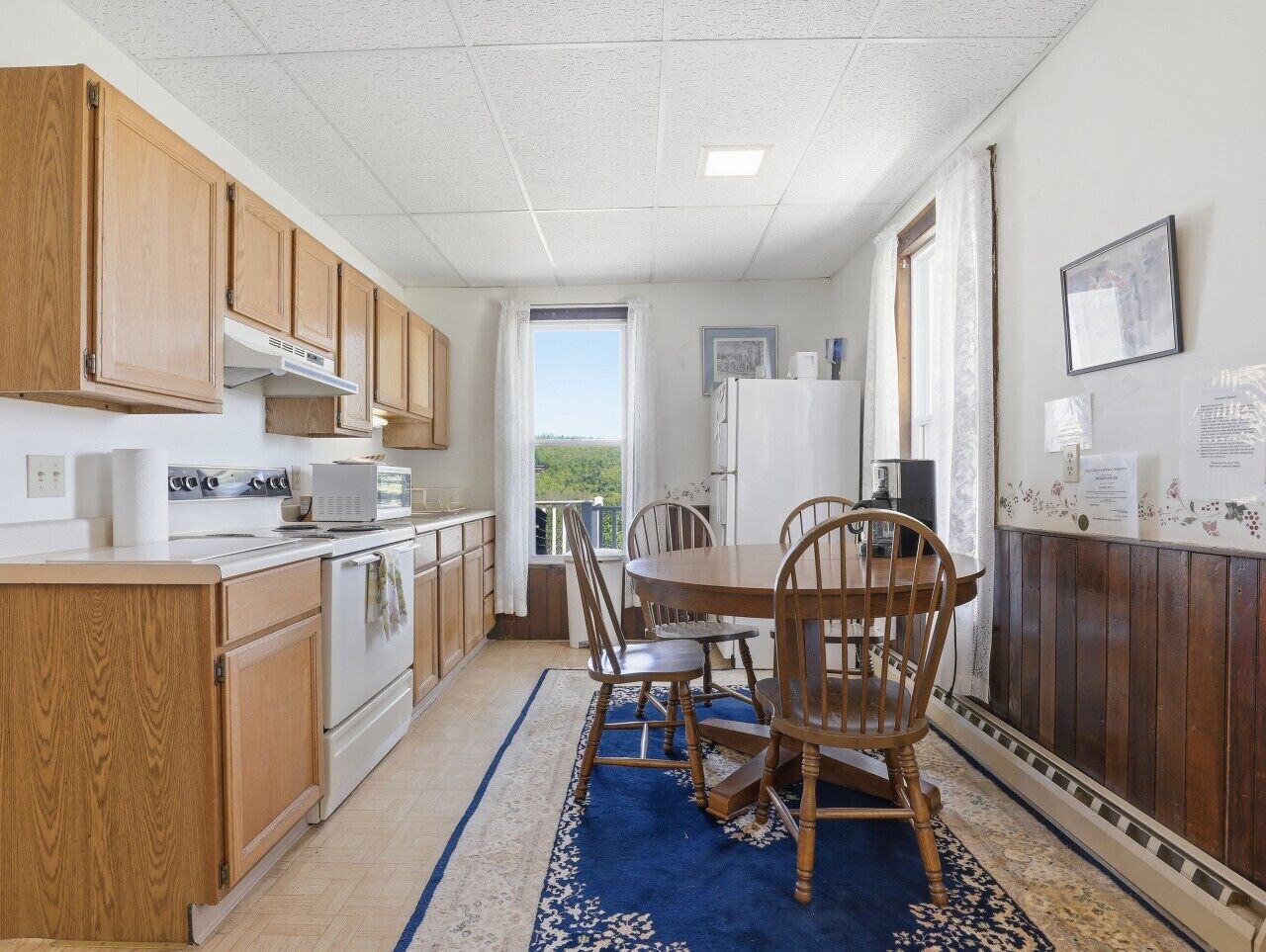 Une cuisine de taille réduite, avec des meubles de rangement en bois, une table à manger avec des chaises, et une vue par la fenêtre.