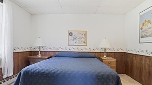Ett sovrum med en säng, två sängbord, en lampa, en vägg med ett blommönster och en inramad tavla.