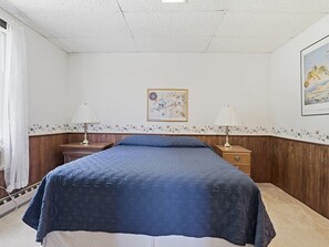 Ein Schlafzimmer mit einem Bett, zwei Nachttischen, einer Lampe, einer Wand mit Blumenmuster und einem gerahmten Bild.