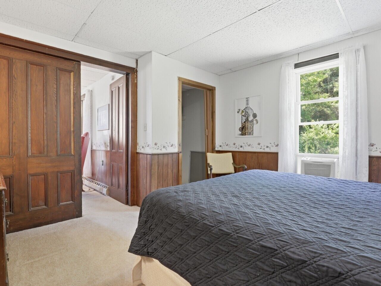 Une chambre à coucher avec un lit, une porte en bois, une fenêtre avec des rideaux et une porte ornée de motifs floraux.
