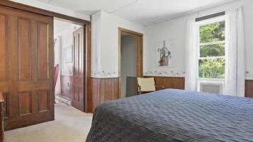 Une chambre à coucher avec un lit, une porte en bois, une fenêtre avec des rideaux et une porte ornée de motifs floraux.
