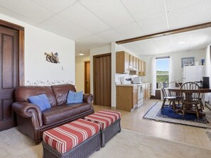 Ein gemütliches Wohnzimmer mit einer braunen Ledersofa, einem gestreiften Ottomanen und einem Essbereich mit Holztischen und einer Tischplatte.