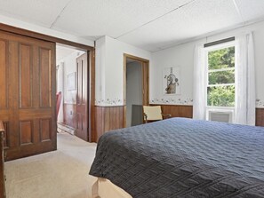 A bedroom with a bed, a wooden door, a window with curtains, and a door with a floral design.
