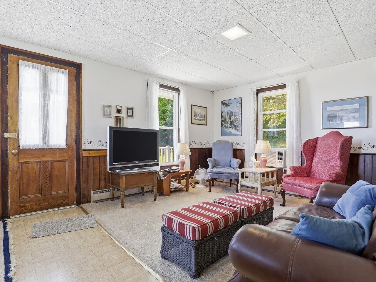 A living room with a television, two armchairs, a sofa, a small table, and a door.