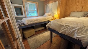 Ett sovrum med två sängar, ett fönster med gardiner, en karta på väggen och en liten lampa.