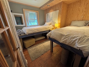 A bedroom with two beds, a window with curtains, a map on the wall, and a small lamp. - Cozy, 3-Bedroom Bungalow just a short walk to beach and sound. (Rodanthe)