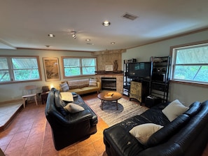 A living room with a fireplace, black leather sofas, a television, and a bookshelf. - Cozy, 3-Bedroom Bungalow just a short walk to beach and sound. (Rodanthe)