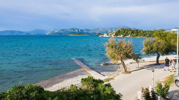 Vista sulla costa con acqua limpida, una spiaggia sabbiosa e una piccola isola con alberi.