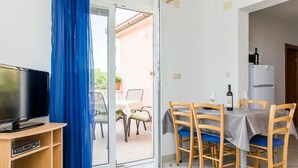 Una stanza con televisione, un tavolo da pranzo con sedie, un frigorifero e una tenda blu.