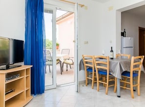 Ein Zimmer mit Fernseher, einem Esstisch mit Stühlen, einem Kühlschrank und einem blauen Vorhang.