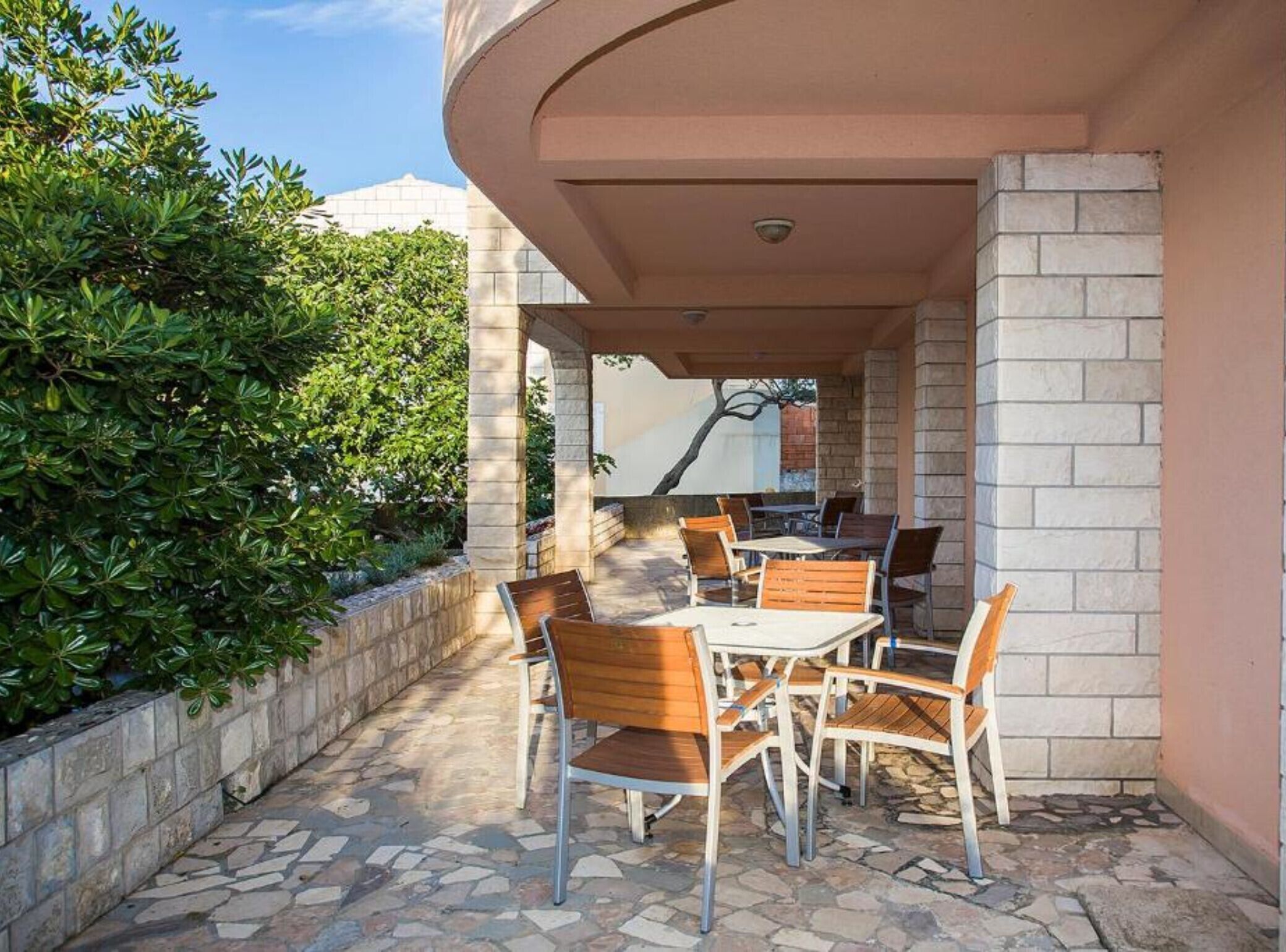 An outdoor patio with stone flooring, wooden tables and chairs, and a stone wall on one side.