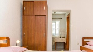 Ein Schlafzimmer mit einem hölzernen Kleiderschrank, einem Bett mit rosa Bettwäsche und einem durch eine offene Tür einsehbaren Badezimmer.