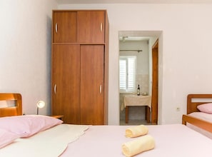 Ein Schlafzimmer mit einem hölzernen Kleiderschrank, einem Bett mit rosa Bettwäsche und einem durch eine offene Tür einsehbaren Badezimmer.