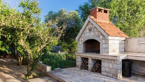 Cucina esterna in pietra con un camino in mattoni, immersa nel verde e con un'area pavimentata in pietra.