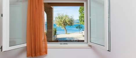 Ein Schlafzimmer mit offenem Fenster, einem Bett und Blick auf einen Strand.
