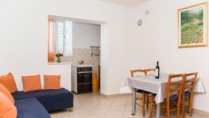 Un ambiente compatto con divano, tavolo da pranzo, sedie, angolo cottura e un quadro appeso al muro.