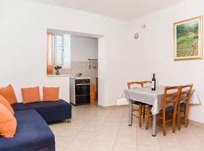 Ein kompakter Wohnbereich mit Sofa, Esstisch, Stühlen, Küchenzeile und einem Bild an der Wand.