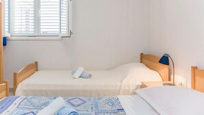 A bedroom with two beds, a window with blinds, a bedside lamp, and a quilt. - one bedroom with balcony and sea view A4 (Janjina)