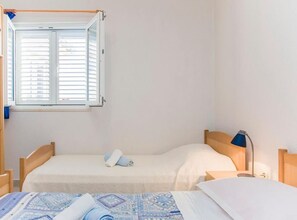 A bedroom with two beds, a window with blinds, a bedside lamp, and a quilt. - one bedroom with balcony and sea view A4 (Janjina)