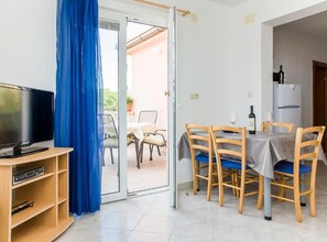 A room with a television, a dining table with chairs, a refrigerator, and a blue curtain. - one bedroom with balcony and sea view A4 (Janjina)