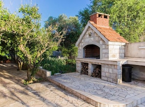 A stone-built outdoor kitchen with a brick chimney, surrounded by greenery and a stone-paved area. - one bedroom with balcony and sea view A4 (Janjina)