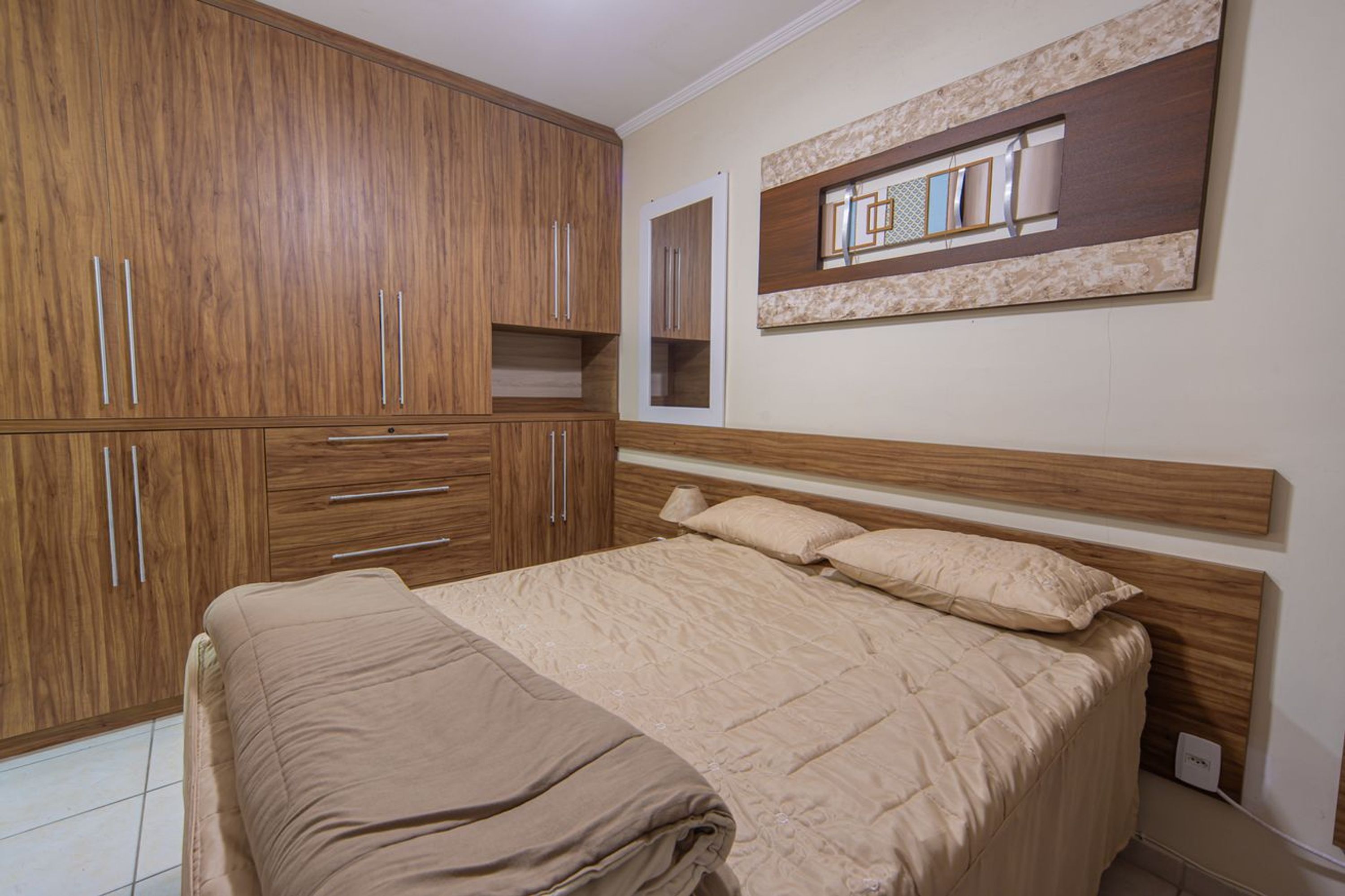 A bedroom with a bed, wooden wardrobe, and a wall-mounted mirror.