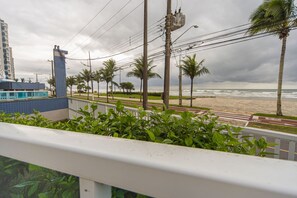 A coastal view with a beach, palm trees, and a building with blue and white tiles. - Apto c Varanda Vista Mar p 6 Pessoas em Cai ara (Praia Grande)