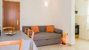 Un salon comprenant un canapé, des fauteuils, une table et un coin cuisine.