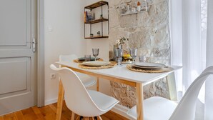 Un espace repas avec une table blanche, des chaises et un mur en pierre en arrière-plan.