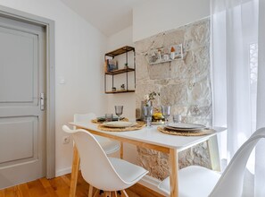 A dining area with a white table, chairs, and a stone wall backdrop. - Classic Studio Apartment (Komiza)