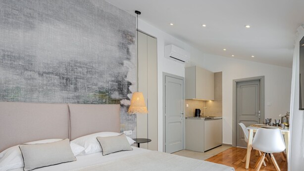 Une chambre moderne avec un grand lit, des tables de chevet, une lampe et une vue sur un coin cuisine et un espace repas.