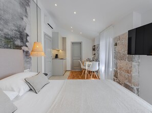 A modern bedroom with a large bed, a small kitchenette, a dining area, and a stone accent wall. - Classic Studio Apartment (Komiza)