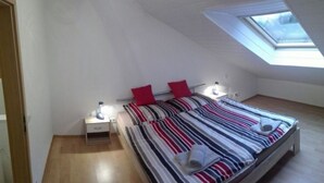 Una camera da letto con un lucernario, un letto con lenzuola a righe, un comodino e un pavimento in legno.