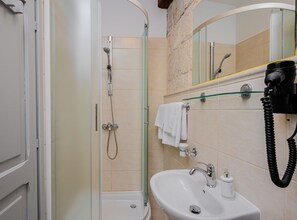 A bathroom with a glass shower enclosure, a sink with a mirror, and a hairdryer mounted on the wall. - Studio Apartment with Balcony (Komiza)