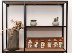 A shelf with decorative items including a vase with dried flowers, two potted plants, and a wooden display of stones. - Studio Apartment with Balcony (Komiza)