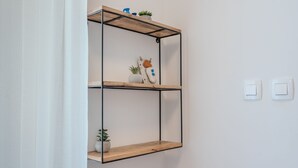 Un estante metálico fijado a la pared con dos niveles, cada uno con adornos y una planta en maceta.