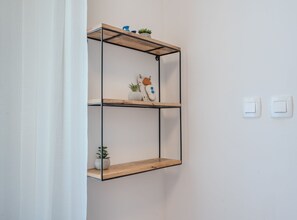 A wall-mounted metal shelf unit with two levels, each holding decorative items and a potted plant. - Comfort Studio Apartment (Komiza)
