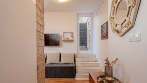 Un pasillo con un sofá, piso de madera, una escalera, un espejo montado en la pared y una pequeña mesa con una planta.