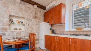 Una cocina con armarios de madera, un refrigerador blanco, una mesa de comedor con sillas azules y una pared de piedra.