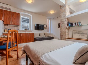 Ein kleiner Wohnbereich mit Küchenzeile, Essplatz, Sofa, Bett und einer Ziegelwand.