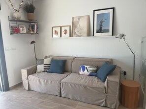 A neutral-toned sofa with blue and striped cushions, a floor lamp, and wall-mounted shelves with decorative items and framed pictures. - House with large swimming pool 1 minute 30 walk from the beach (Santiago de la Ribera)