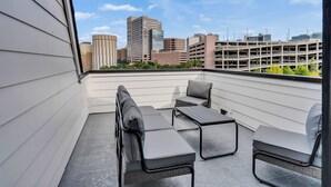 A rooftop terrace with a seating area, a view of the cityscape, and a parking garage in the background. - Brand NEW Modern Stay Near Med Center, NRG, Downtown, & more (Houston)