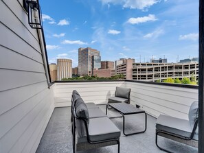 A rooftop terrace with a seating area, a view of the cityscape, and a parking garage in the background. - Brand NEW Modern Stay Near Med Center, NRG, Downtown, & more (Houston)