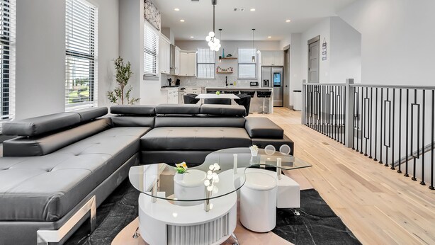 A modern living room with a sectional sofa, a glass coffee table, and a kitchen in the background. - Brand NEW Modern Stay Near Med Center, NRG, Downtown, & more (Houston)