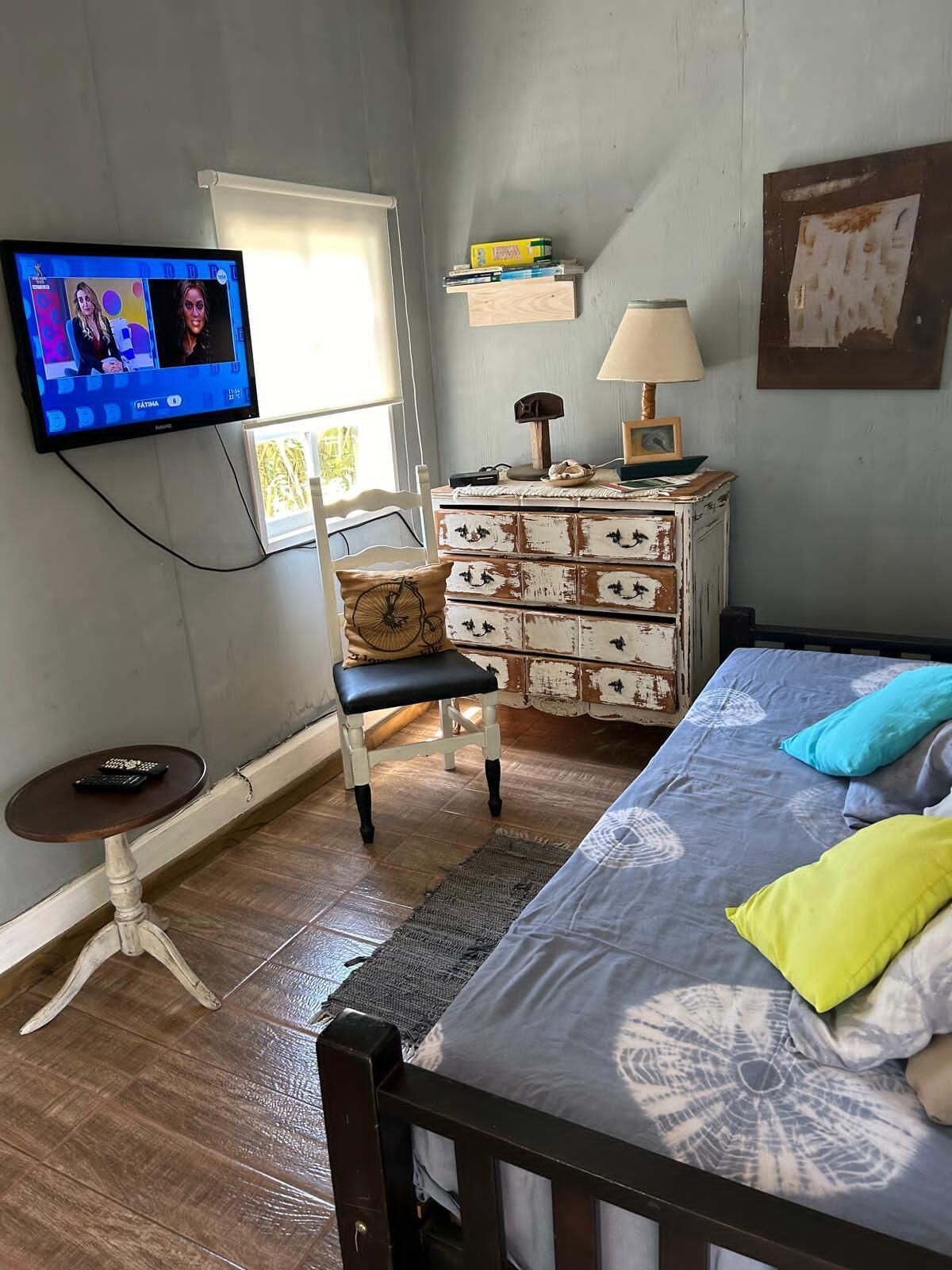 Ein Schlafzimmer mit Bett, Sessel, Kommode, Fernseher und Fenster.
