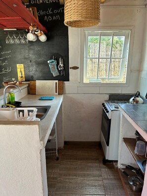 Cocina compacta con estufa a gas, lavamanos y ventana que da a vistas de bambú.