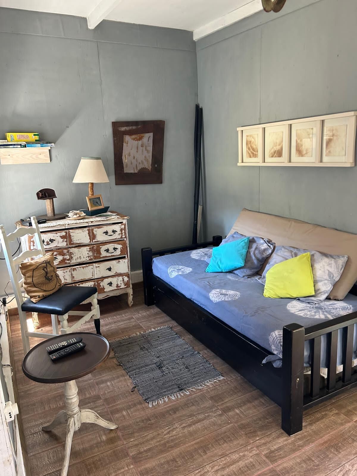 A bedroom with a bed, a dresser, a chair, a table, and a wall with pictures.