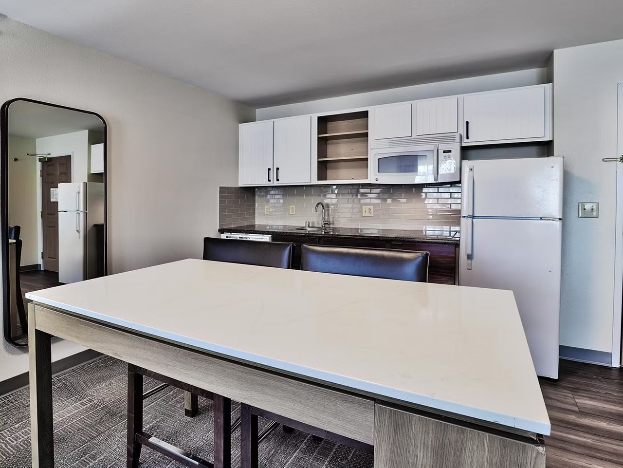 A modern kitchen with white cabinets, a microwave, a refrigerator, and a dining table with chairs.